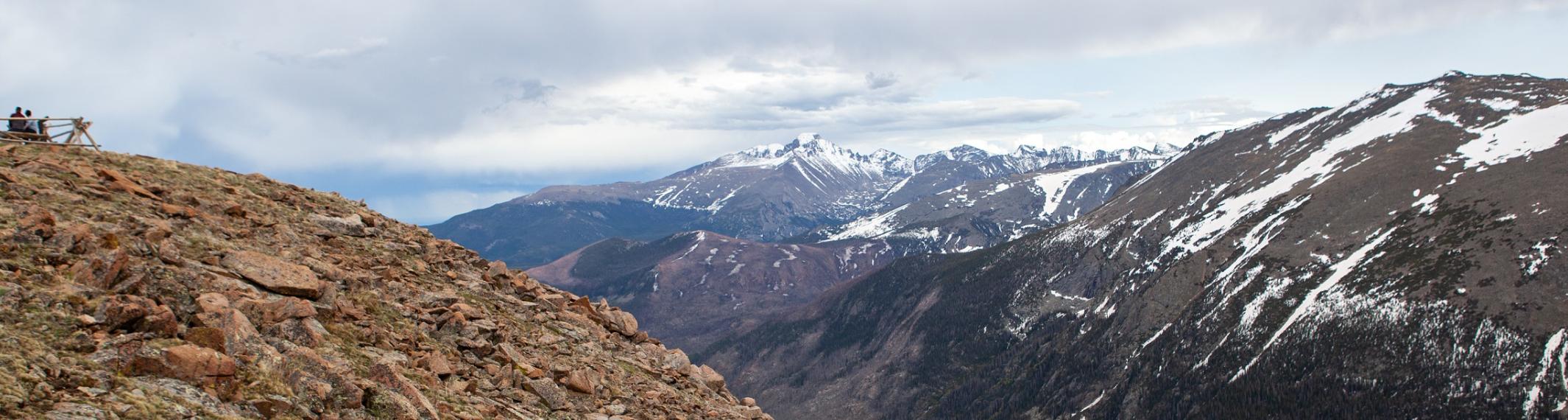 People on top of a rocky peak, take photos of a snowcapped mountain range in the distance