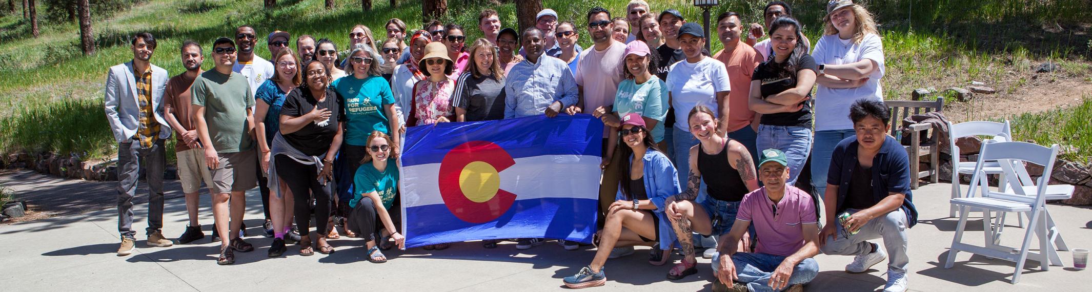 A large diverse group of people holding the Colorado flag in a mountain setting