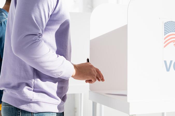 A person in a purple sweater holding a pen at a voting booth