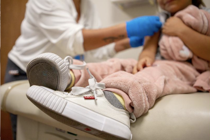 A kindergarten-age girl on an exam table being checked by a nurse