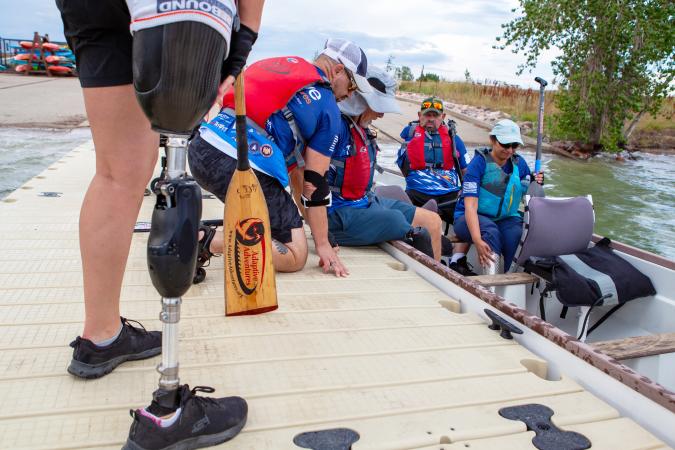 People in personal flotation devices loading into a boat from a dock at a lake